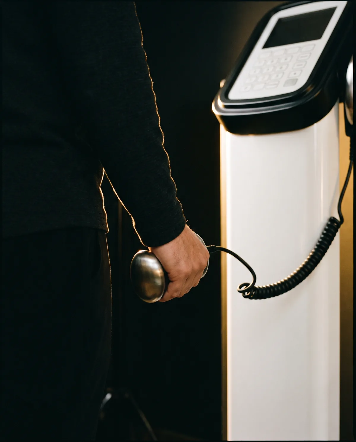 A hand gripping the steel electrode of a body-composition analyser, its coiled cable running back to the instrument